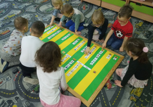 Przedszkolaki siedzą na dywanie i zaznaczają na tablicy zdobyte umiejętności.